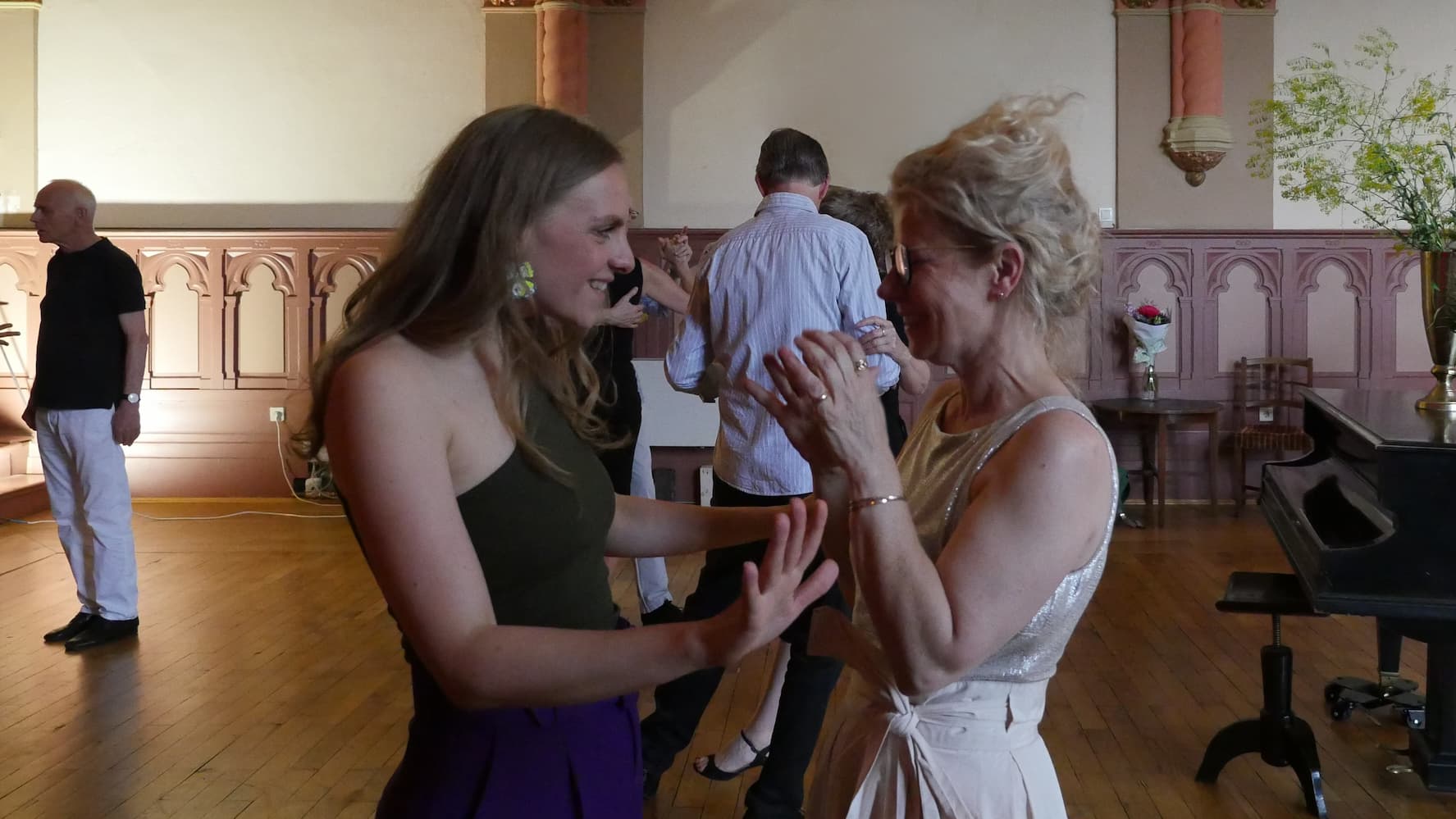 Tango teacher Juliana laughing joyfully with a student in conversation, with further dance couples in the background