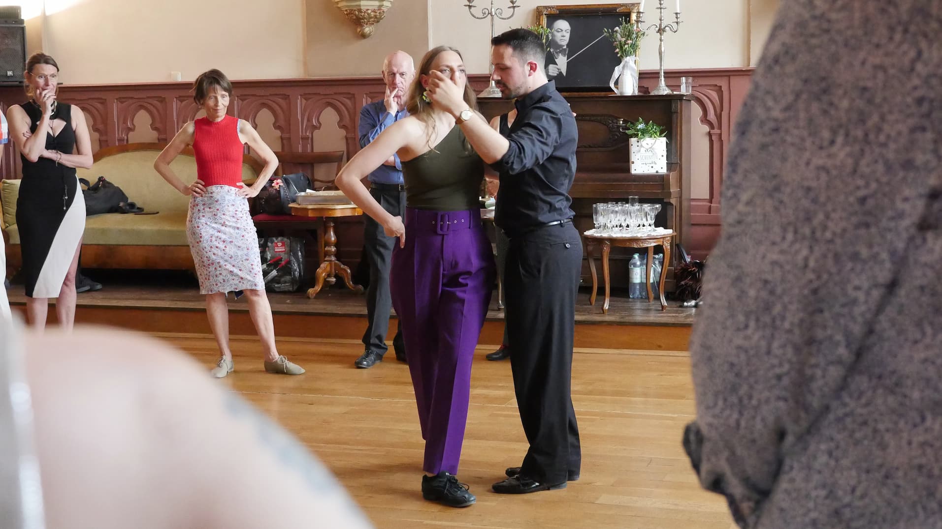 Tango teachers Juliana & Fadi explain precisely and demonstrate something with equal strength and presence, with students around them listening attentively