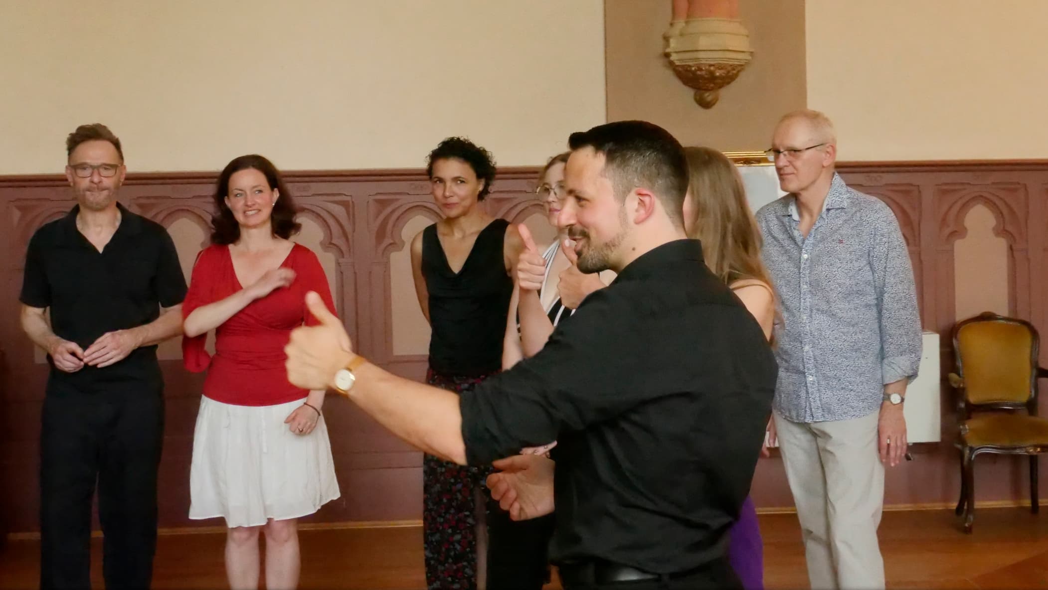 Tango teacher Fadi looks at a student and gives a thumbs up, with further students in the background listening and enjoying themselves